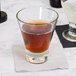 A Libbey customizable rocks glass filled with brown liquid on a table next to a napkin with a water glass.