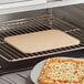 A rectangular pizza stone with a pizza cooking in an oven.