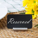 A Tablecraft stainless steel cylinder card holder with a black and white sign reading "reserved" in it.
