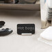 A stainless steel cylinder card holder on a counter with a black sign reading "hot dogs"