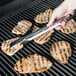 A person holding an Edlund heavy-duty tongs over meat on a grill.