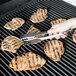 A person using Edlund heavy-duty tongs to grill meat.