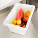 A Rubbermaid white polyethylene food storage container filled with fruit on a counter.
