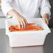 A hand reaching into a white Rubbermaid food storage container filled with carrots.
