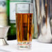 A close up of a Fineline clear plastic cordial shot glass filled with amber liquid on a table.