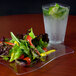 A Fineline clear plastic square plate with a salad next to a glass of water.