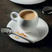 A white Chef & Sommelier bone china coffee cup on a saucer with a spoon.