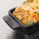 An American Metalcraft mini cast iron rectangular casserole dish filled with cheese and vegetables on a counter.