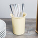A yellow Cal-Mil flatware cylinder full of silverware.