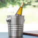 A Vollrath silver metal wine bucket holding a bottle of wine on a table.