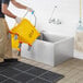A man pushing a yellow bucket into a Regency stainless steel mop sink.