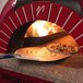 A pizza on a GI Metal square perforated pizza peel with a long handle being cooked in a pizza oven.