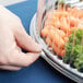 A hand holding a WNA Comet clear plastic container filled with carrots and lettuce.