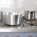 A Vollrath Arkadia sauce pan on a stove with other pots.