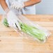 A person wearing gloves holding a plastic bag of celery.
