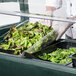 A Carlisle portable salad bar filled with lettuce and spinach on a counter.