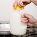 A hand pouring white milk into a Tablecraft PP48J jar.