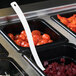 A white plastic spoon in a tray of food on a salad bar counter.