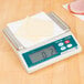 A Taylor digital portion scale on a counter with cheese on it.