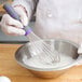 A person using a Vollrath Jacob's Pride stainless steel whisk to mix liquid ingredients in a bowl.