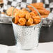 A Tablecraft galvanized steel pail filled with fried food on a table.