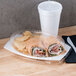 A wrap sandwich in a Dart plastic container on a table with a white plastic cup and a clear plastic dome lid.
