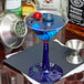 A blue drink in a Fineline Flairware plastic martini glass with a cobalt blue base and a cherry on top.