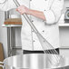 A chef using a Carlisle stainless steel French whisk to stir a large metal pot.