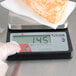 A gloved hand uses a Taylor digital portion control scale to weigh cheese.