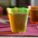 A neon yellow Fineline hard plastic shot cup filled with green liquid on a table.