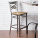 A Lancaster Table & Seating metal cross back bar stool with a driftwood seat next to a table.