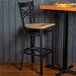 A Lancaster Table & Seating black cross back bar stool with a wooden seat at a table with pizza.