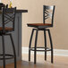 A pair of Lancaster Table & Seating black cross back swivel bar stools with antique walnut wood seats.