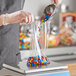 A hand using a metal scoop to pour candy into a plastic bag on a scale.