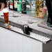 A Regency stainless steel beer drip tray on a bar counter with a glass of beer and bottles.