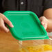 A person holding a green lid over a plastic container of food.