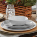 An American Metalcraft white melamine bouillon cup on a table with a white plate.