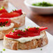 A plate with four slices of bread topped with cream cheese, tomatoes, and fire roasted red pepper strips.