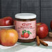 A case of 12 Kime's jars of apple butter spread with apples on a table.