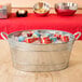 A Tablecraft galvanized steel beverage tub filled with ice and soda cans on a table.