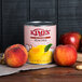 A can of Kime's peach halves on a table next to a can of Kime's peach nectar.