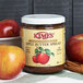 A jar of Kime's Cinnamon Apple Butter spread on a table with red apples.