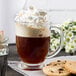 A glass cup of coffee with Cabot whipped cream and cookies on a plate.
