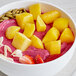 A bowl of fruit smoothie with mango, pineapple, and strawberries.