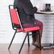 A woman sitting on a Lancaster Table & Seating red stackable chair with a 2" padded seat at a table in a restaurant dining area.