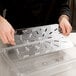 A person using a Cambro clear plastic food box drain tray on a counter.