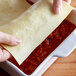 A person holding Seviroli flat lasagna pasta sheets over a baking dish.