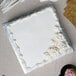 A white cake on a silver square cake board with utensils.