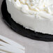 A close up of a black Enjay round cake drum under a cake with white frosting.