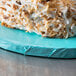 A slice of cake with white frosting and coconut flakes on a blue Enjay round cake board.
